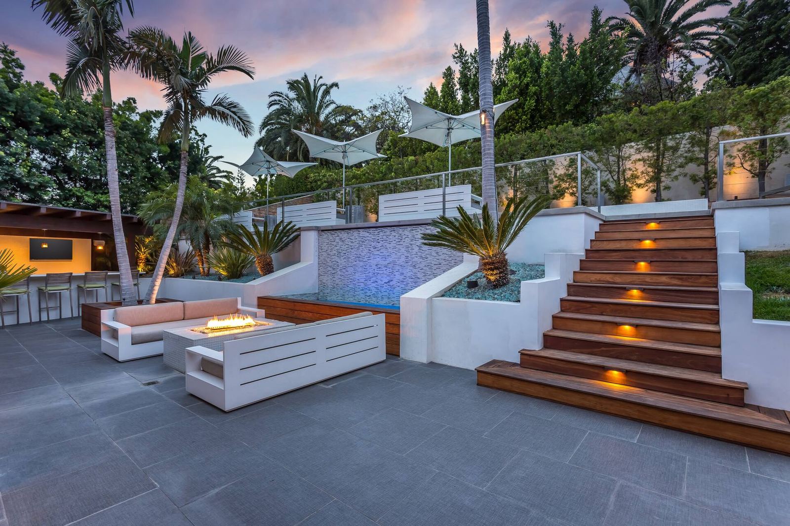 Backyard water feature, lit wooden staircase and fire pit seating at dusk